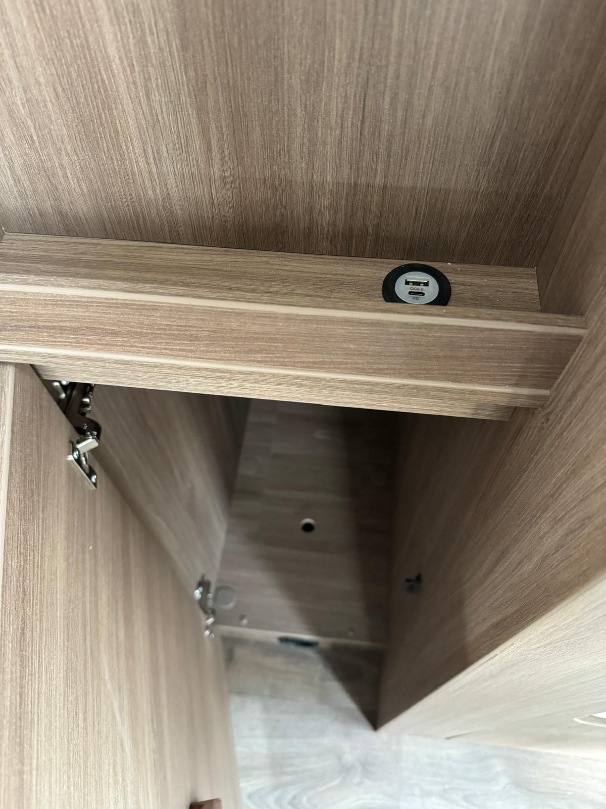 Im Inneren eines Schranks mit heller Holzmaserung sind ein schwarzer, runder Gegenstand und Schrankbeschläge zu sehen.