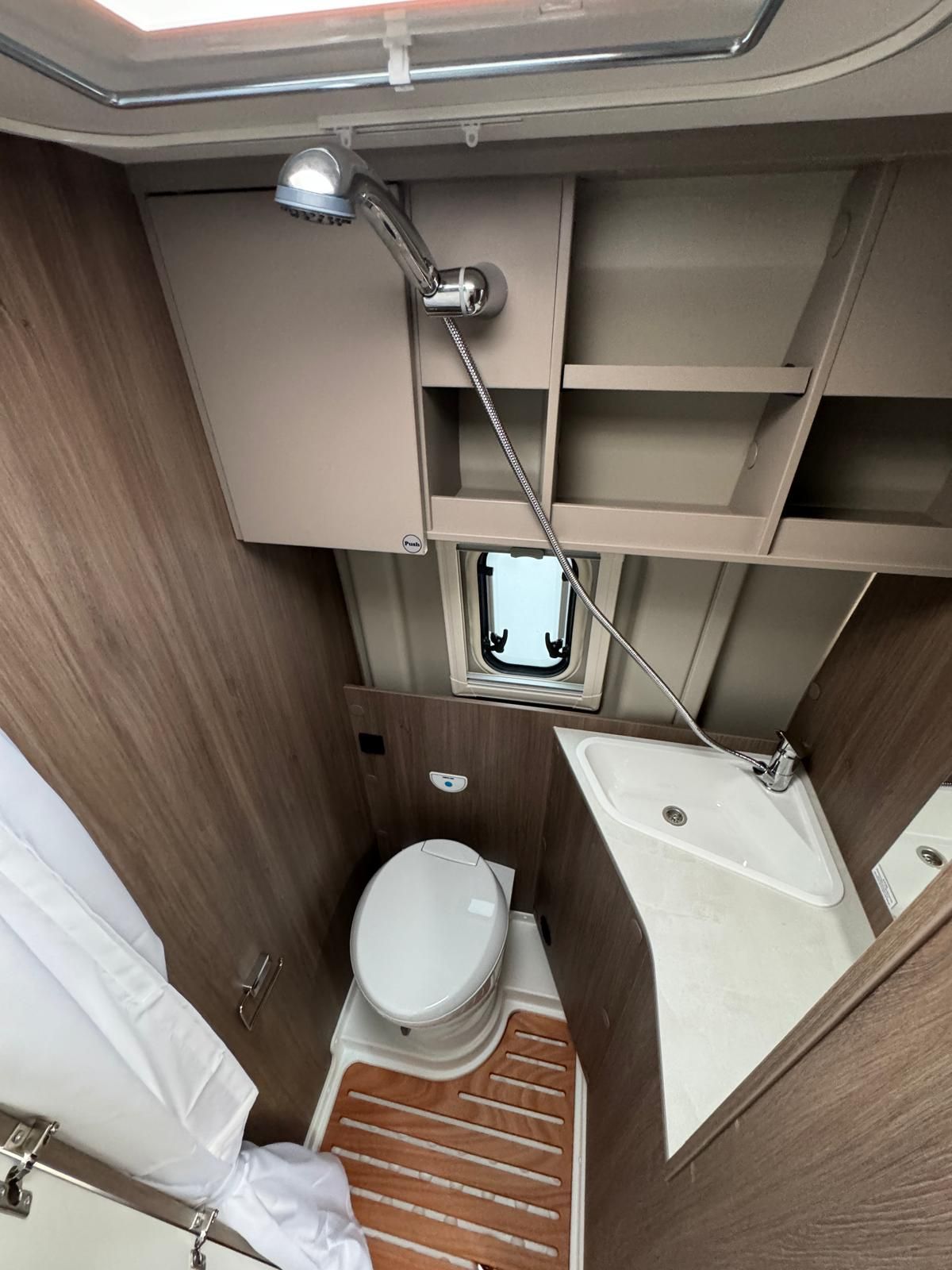 Kleines, geschlossenes Wohnmobil-Badezimmer mit Dusche, Toilette und Waschbecken. Holzelemente und kleines Fenster.