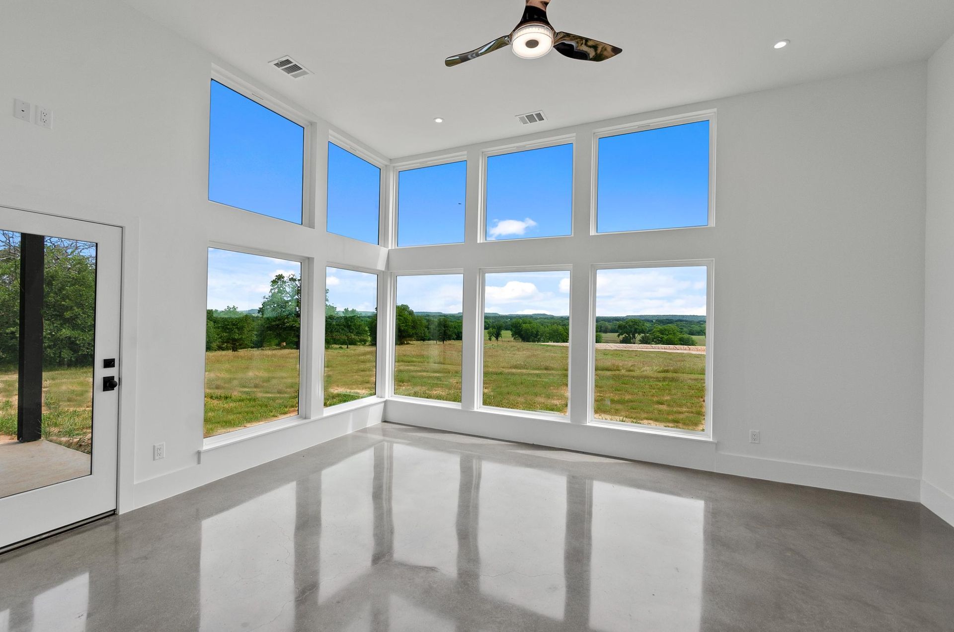 An empty room with a lot of windows and a ceiling fan.