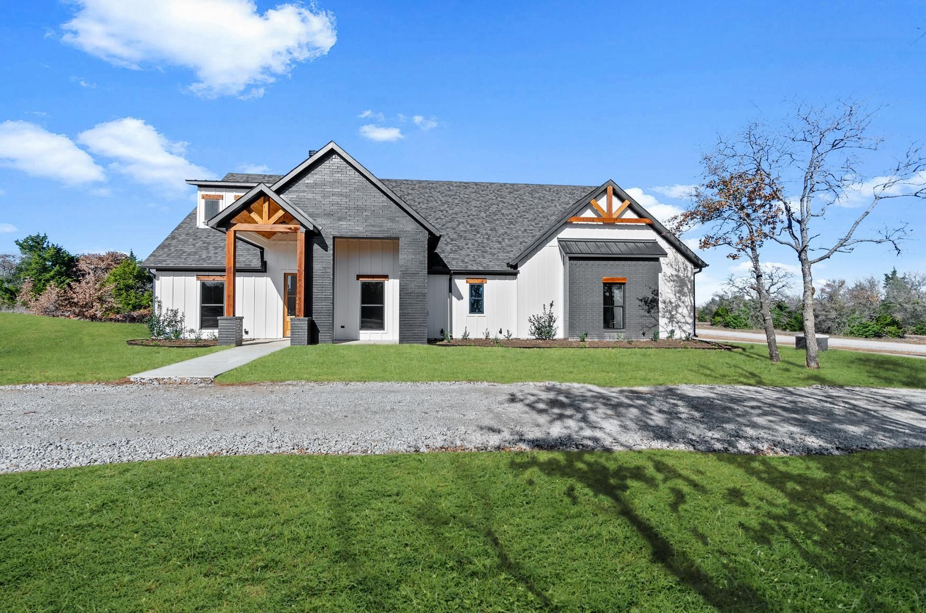 A large white house with a gray roof is sitting on top of a lush green field.