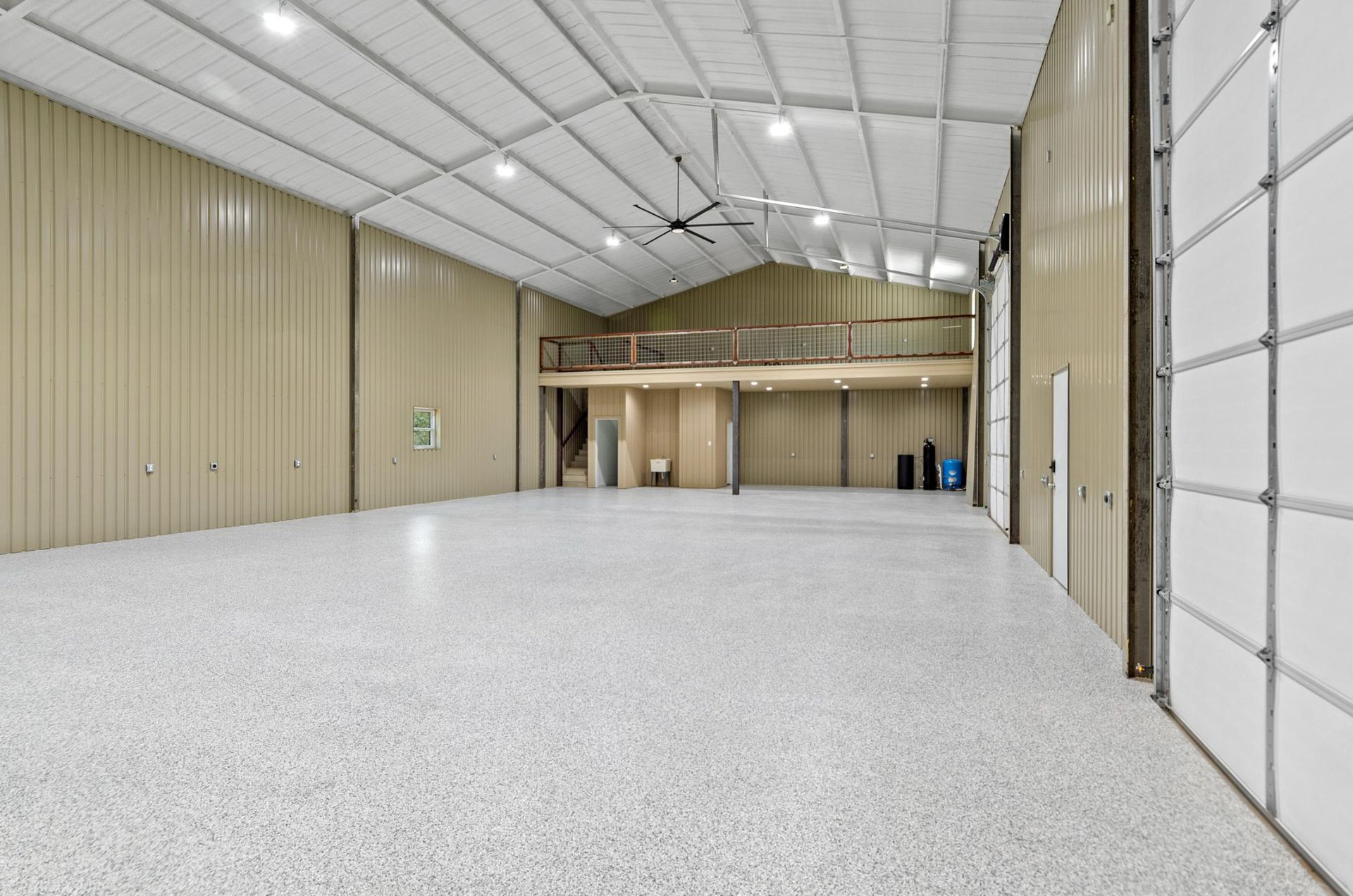 A large empty warehouse with a garage door and a ceiling fan.
