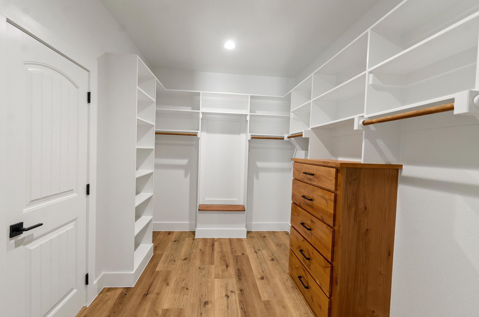 A walk-in closet with hardwood floors and a wooden dresser.