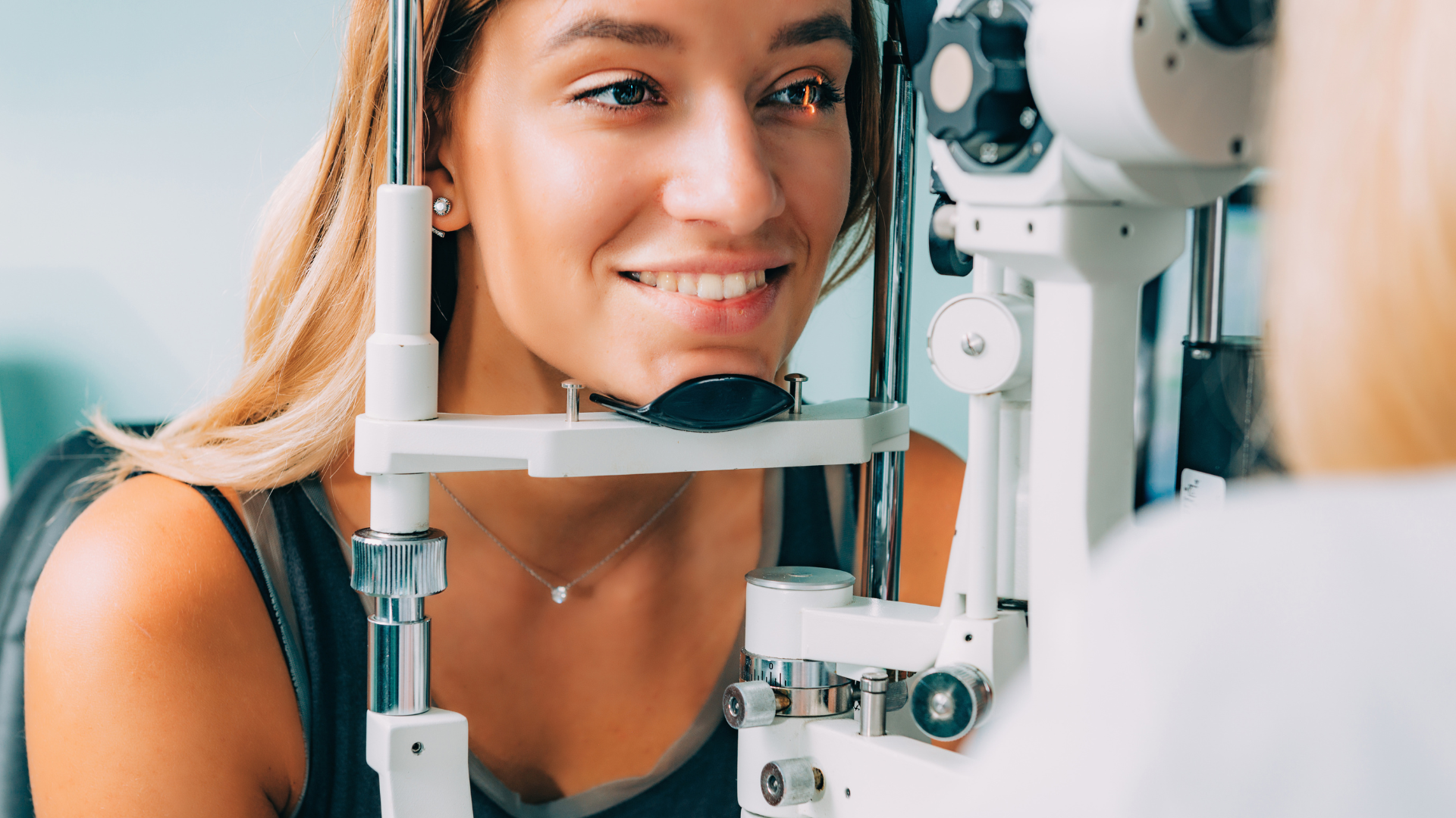 Woman smiling during an eye exam with a slit lamp in an optometrist’s office