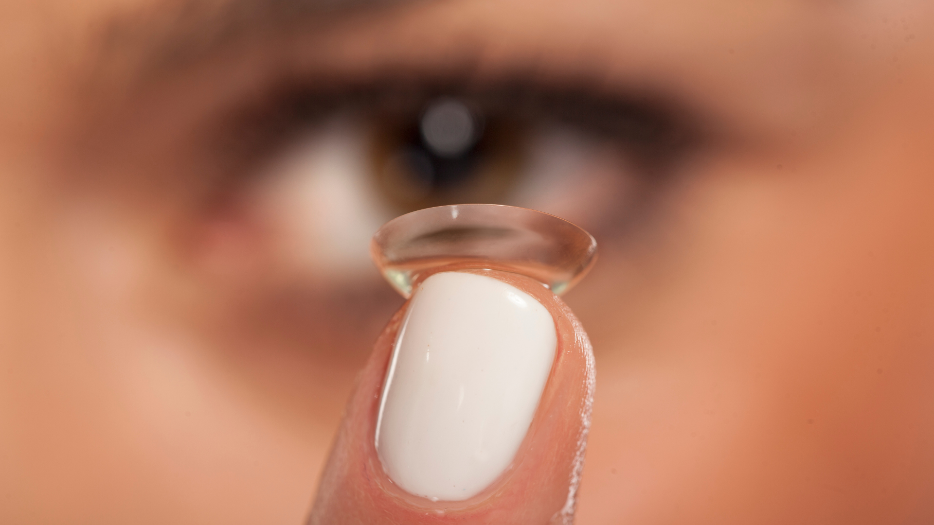 Contact lens held on a fingertip near a blurred eye