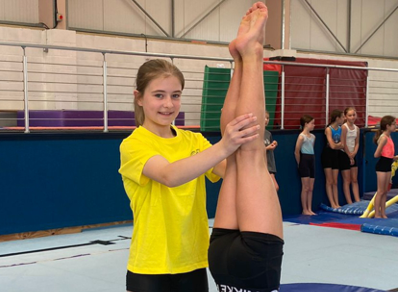 A girl in a yellow shirt is helping a girl do a handstand.