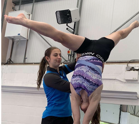 A woman is helping a gymnast do a handstand.