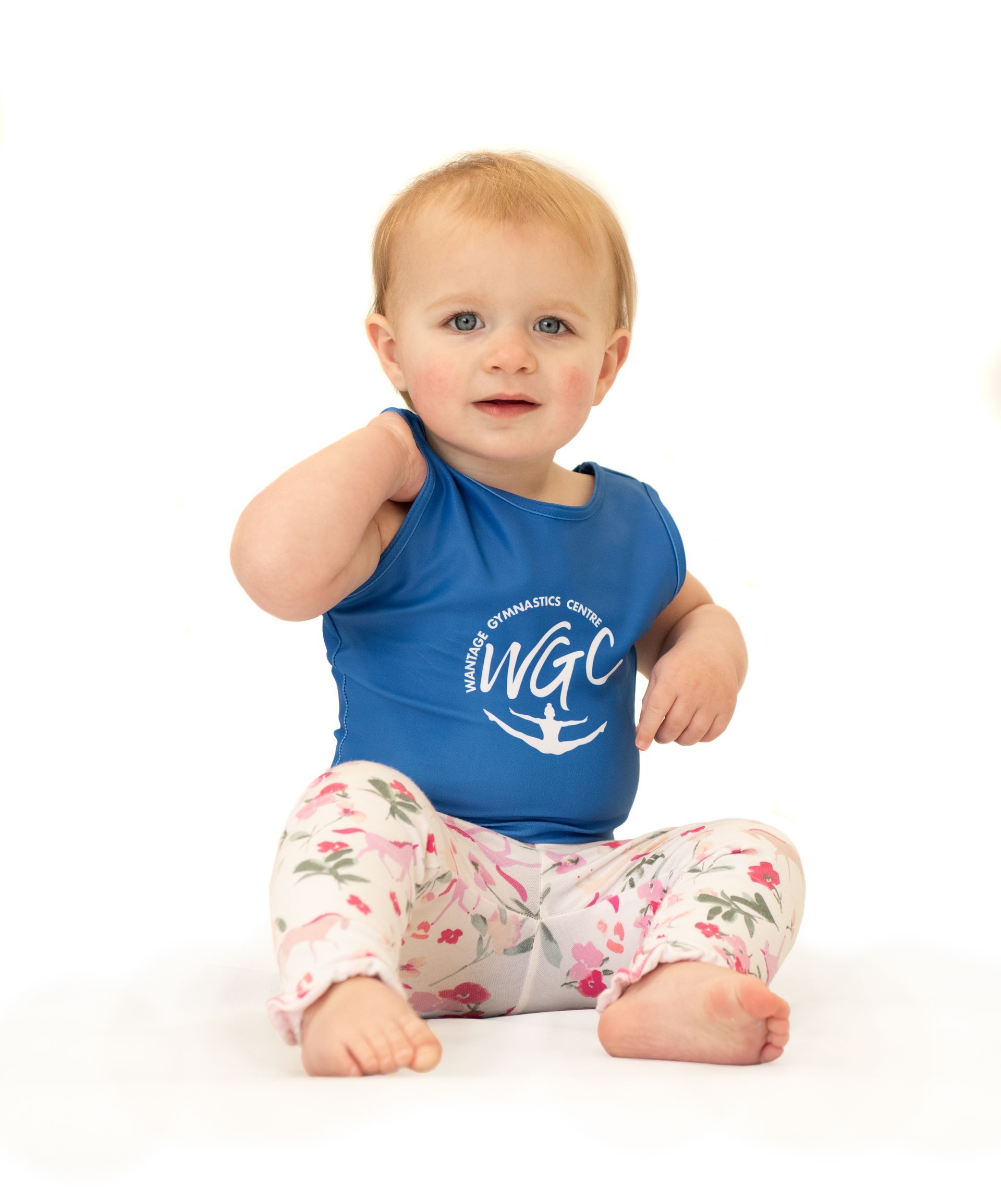 A baby is sitting on the floor wearing a blue shirt and pink pants.