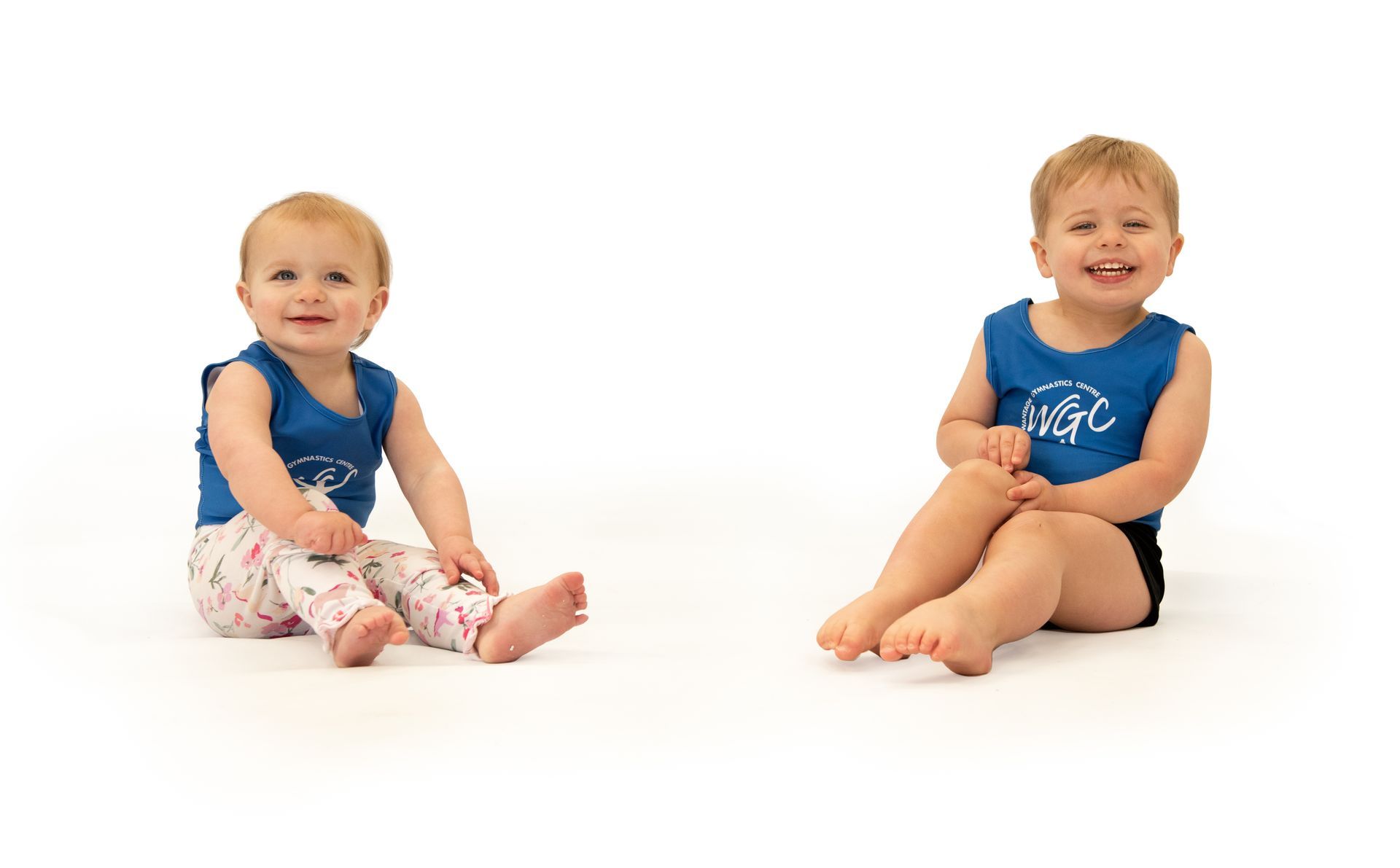 Two babies are sitting next to each other on the floor.