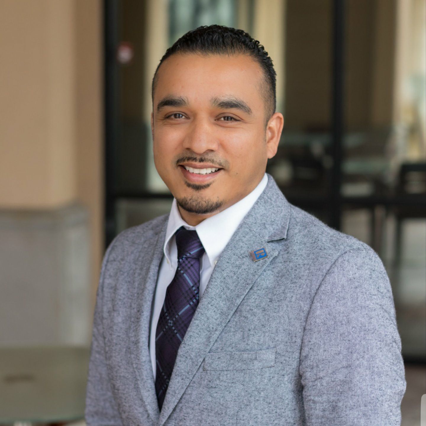 Man in gray suit and tie smiles, standing outside.