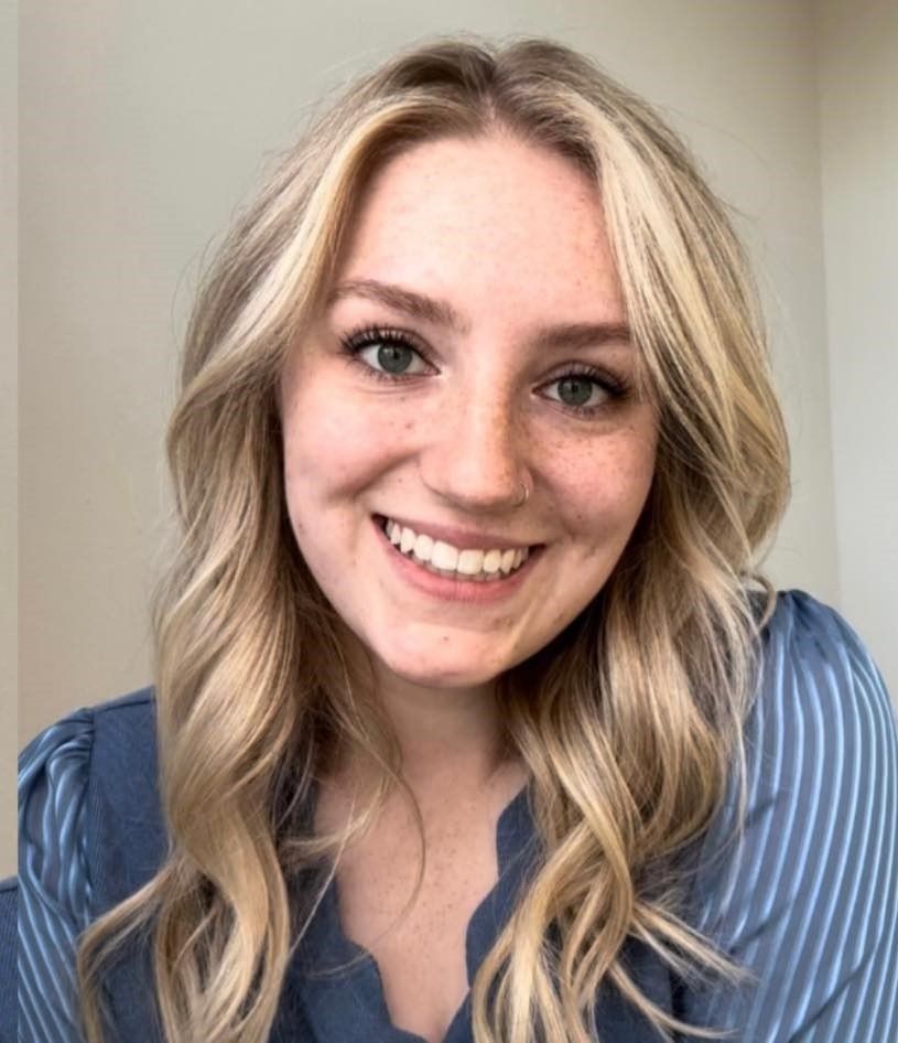 Woman with blonde hair smiles, wearing a blue striped top.