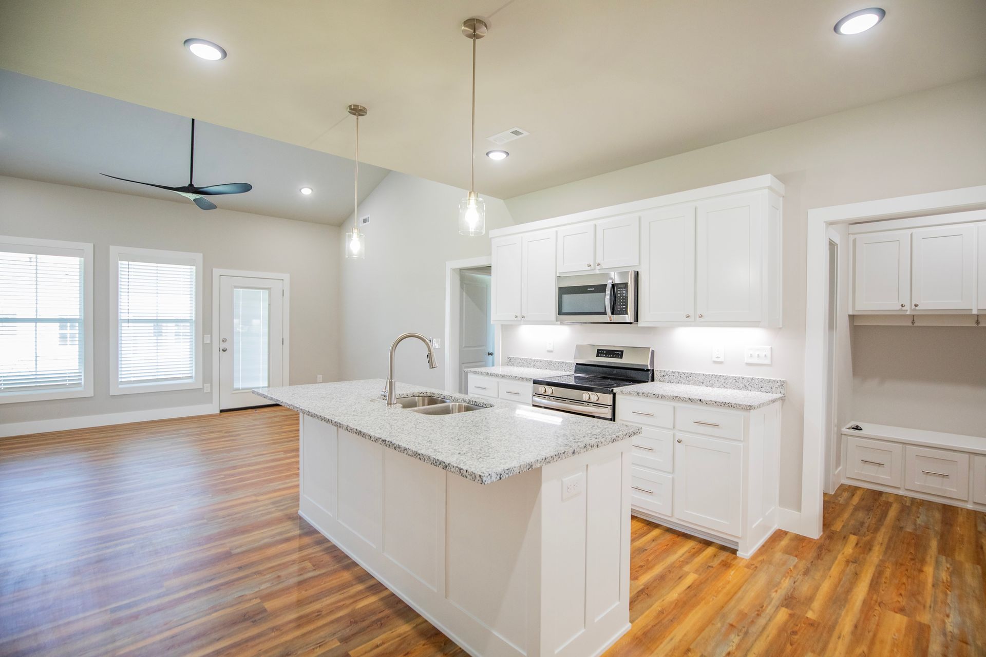 White kitchen with island, cabinets, granite countertops, and hardwood floors.