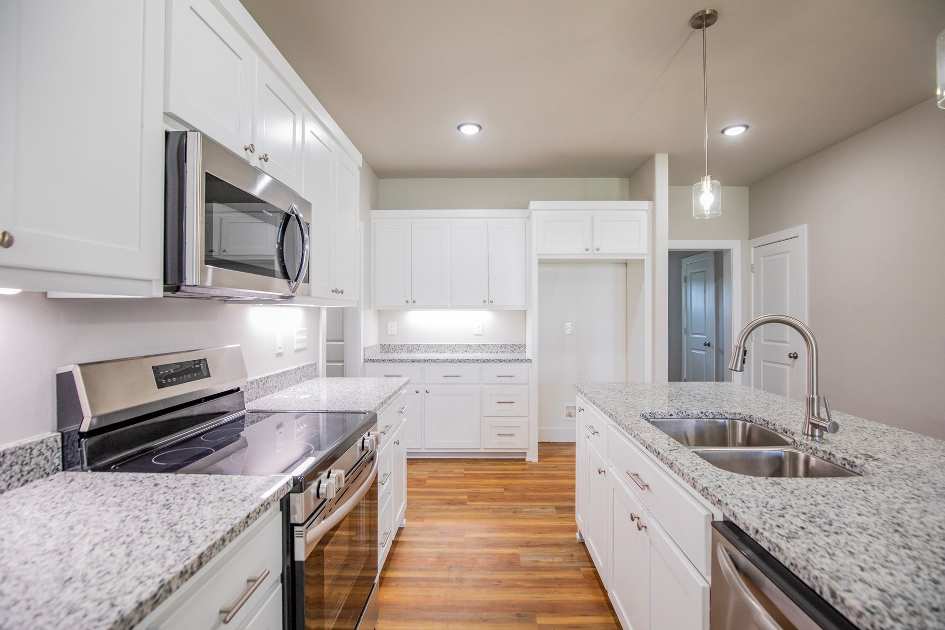 Modern white kitchen with stainless steel appliances, granite countertops, and wooden floors.