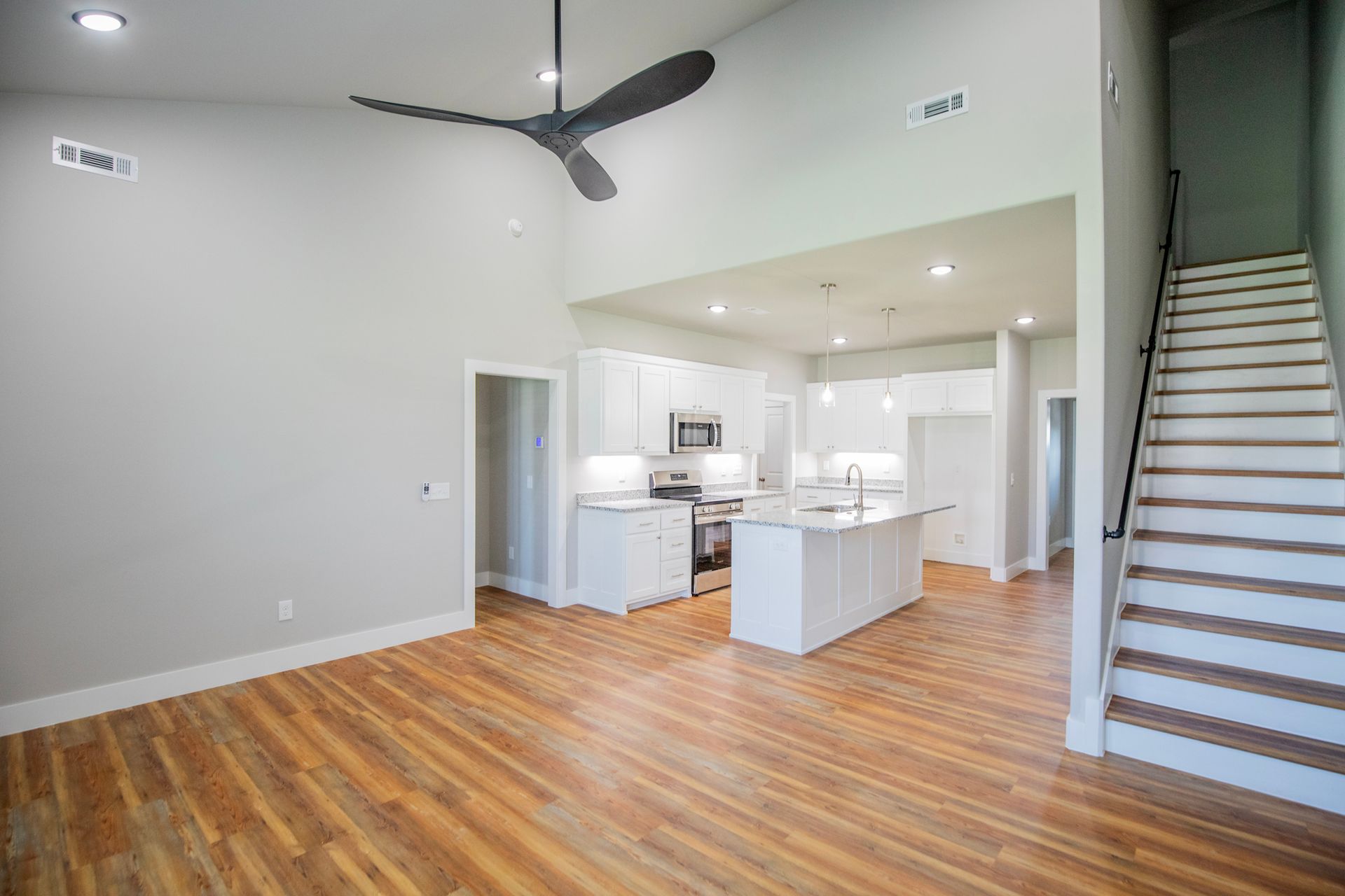 Open-concept kitchen and living area with wood floors, white cabinetry, and a staircase leading upstairs.