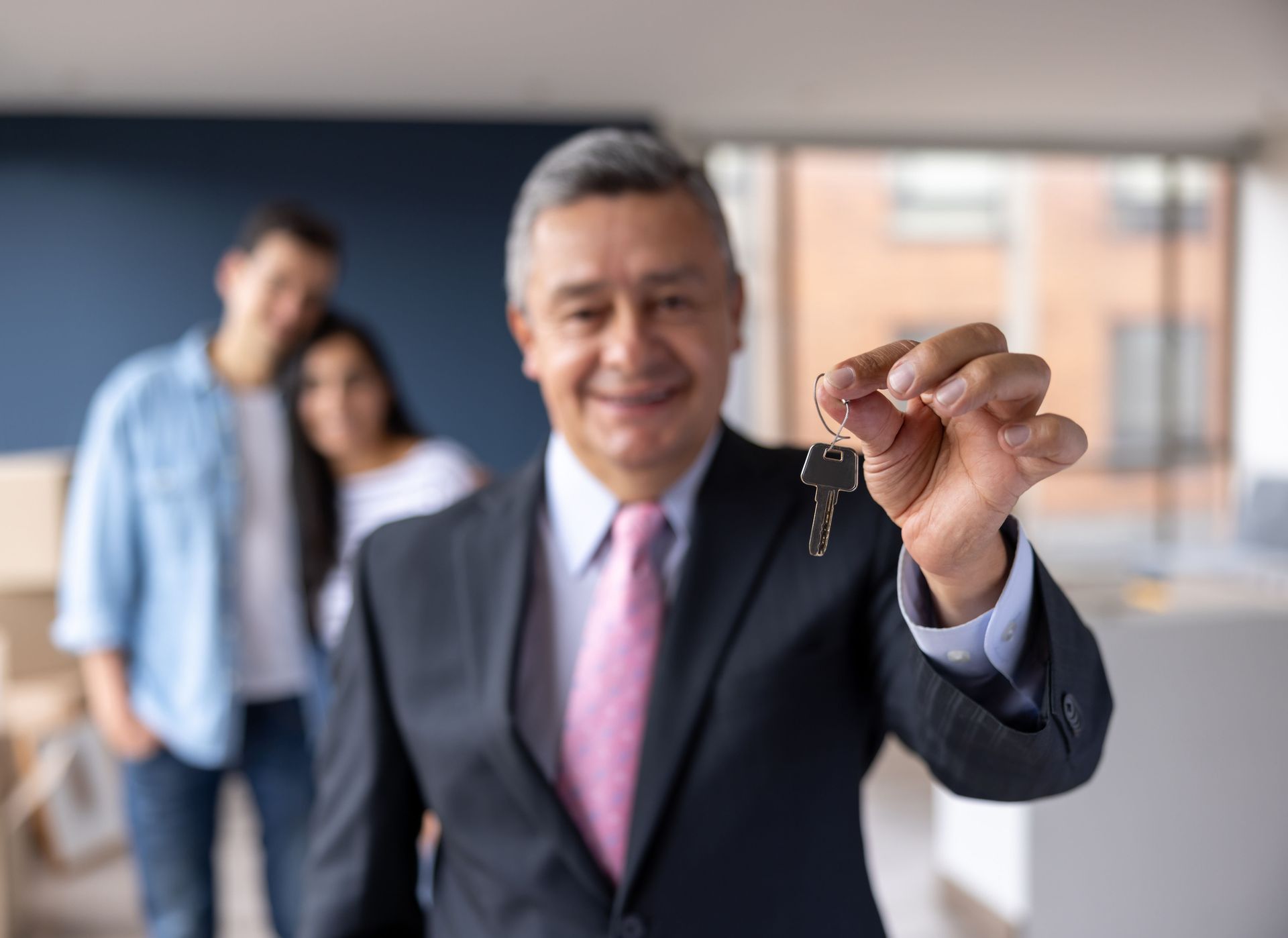 Real estate agent smiling, holding keys; couple in background.