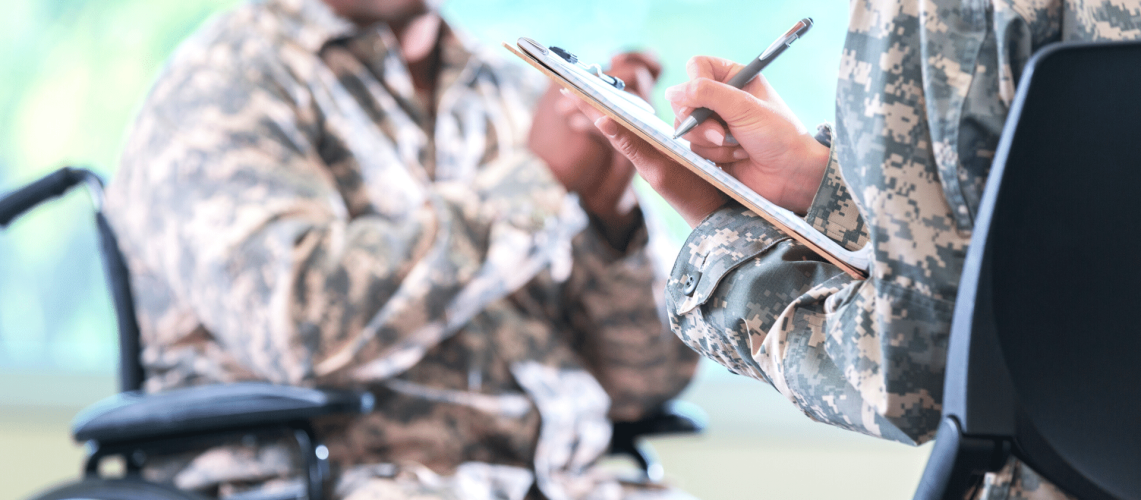 A soldier in a wheelchair is talking to another soldier while holding a clipboard.