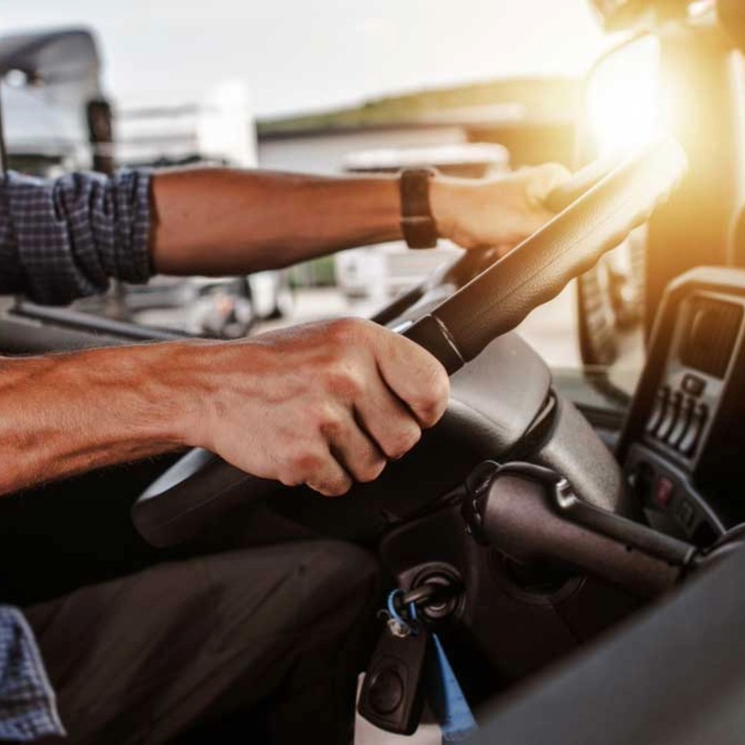 A man is driving a truck with his hands on the steering wheel.