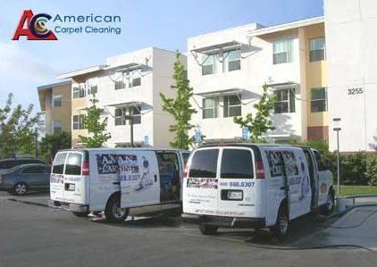 Two american carpet cleaning vans are parked in front of a building