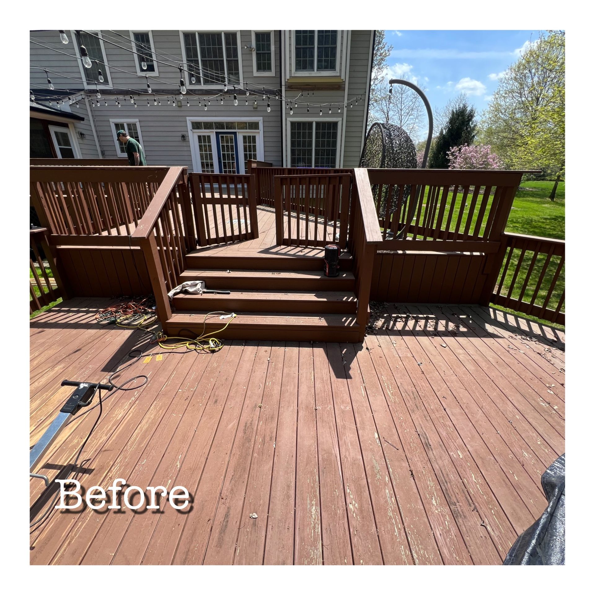 A before picture of a wooden deck with stairs and a house in the background.