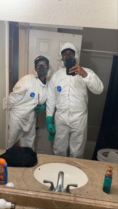 Two men in protective suits are taking a selfie in a bathroom.