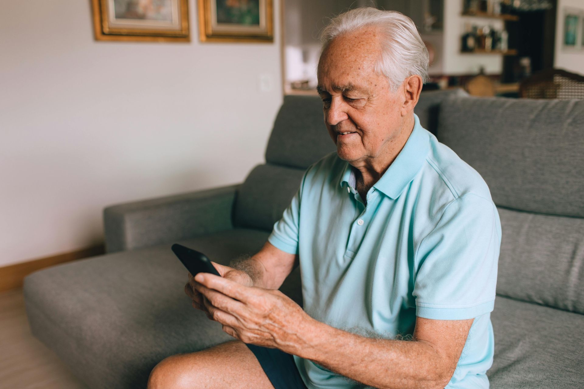 An elderly man is sitting on a couch using a cell phone.