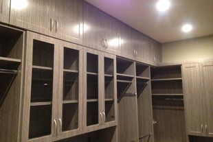 A walk in closet with lots of cabinets and glass doors.