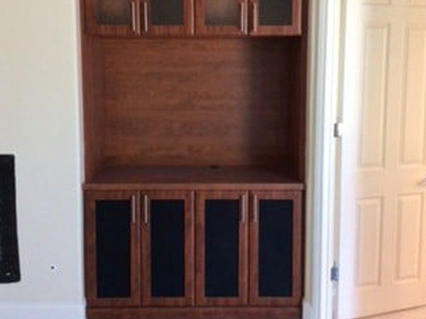 A wooden cabinet with black doors is in a room next to a fireplace.
