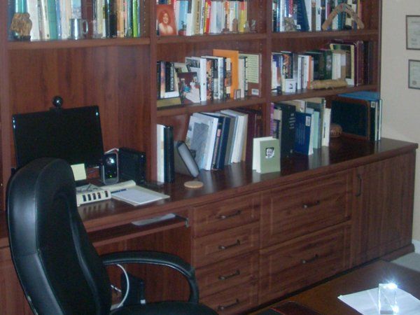 A desk with a computer and a chair in front of a bookshelf