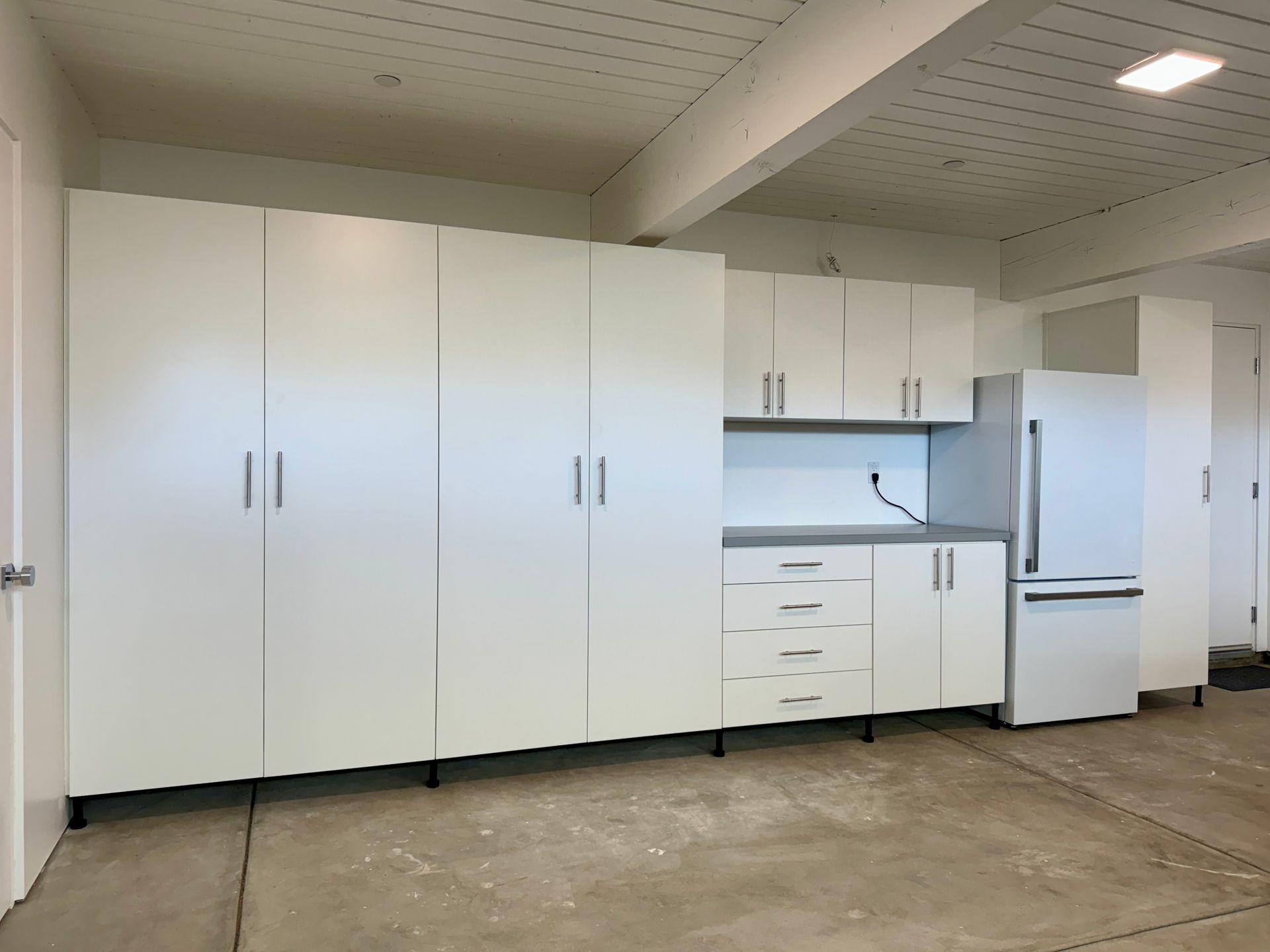 A garage with white cabinets and a refrigerator.