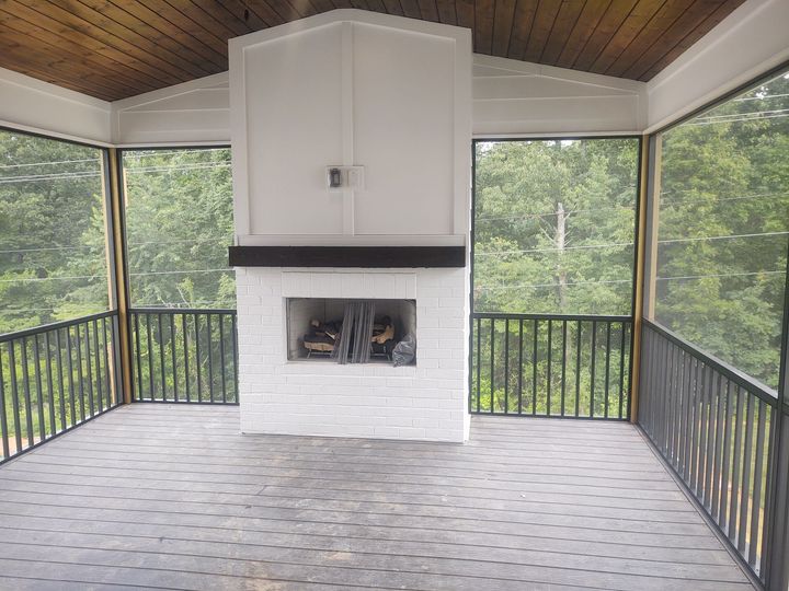 a screened in porch with a fireplace and trees in the background