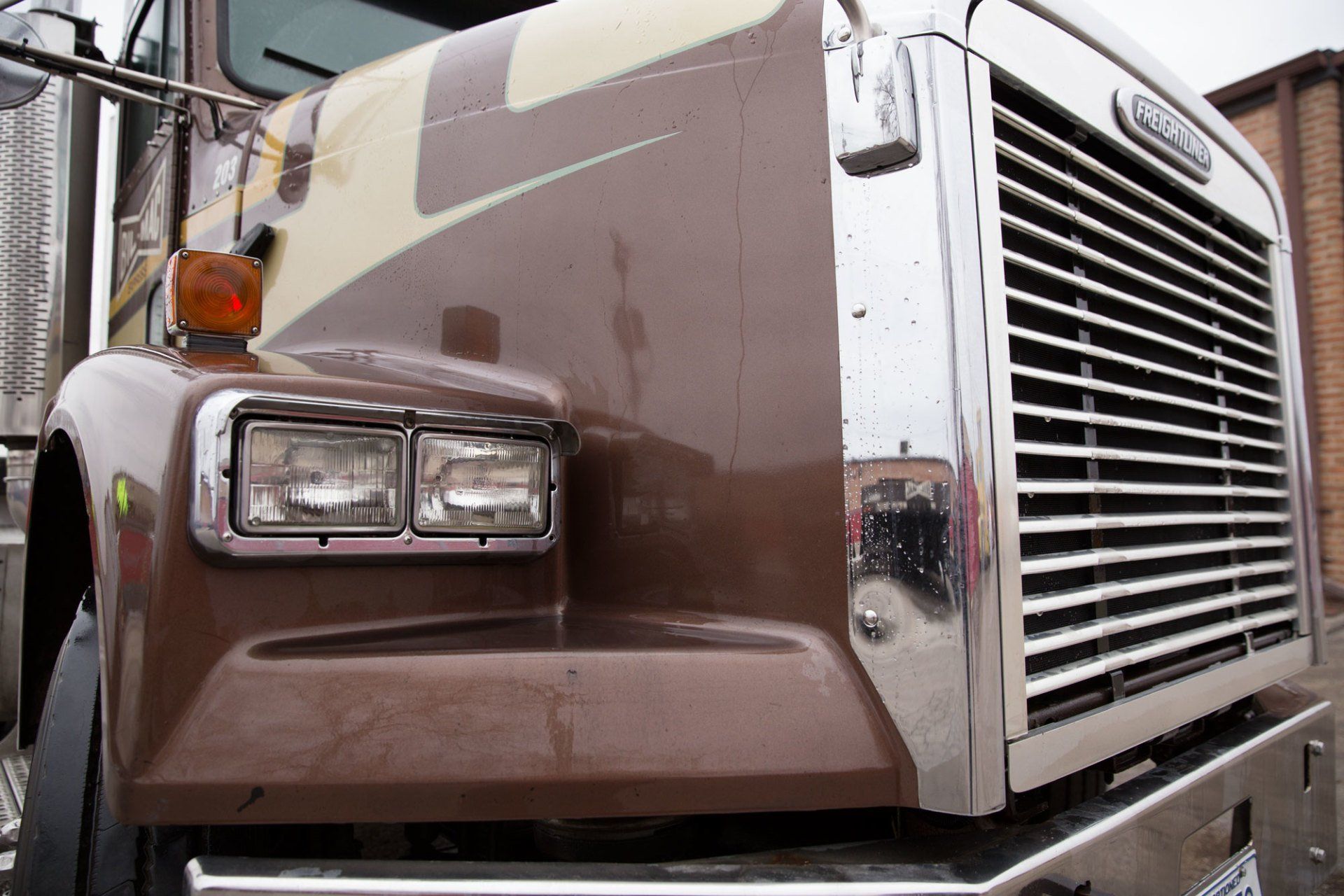 A brown semi truck is parked in front of a brick building.