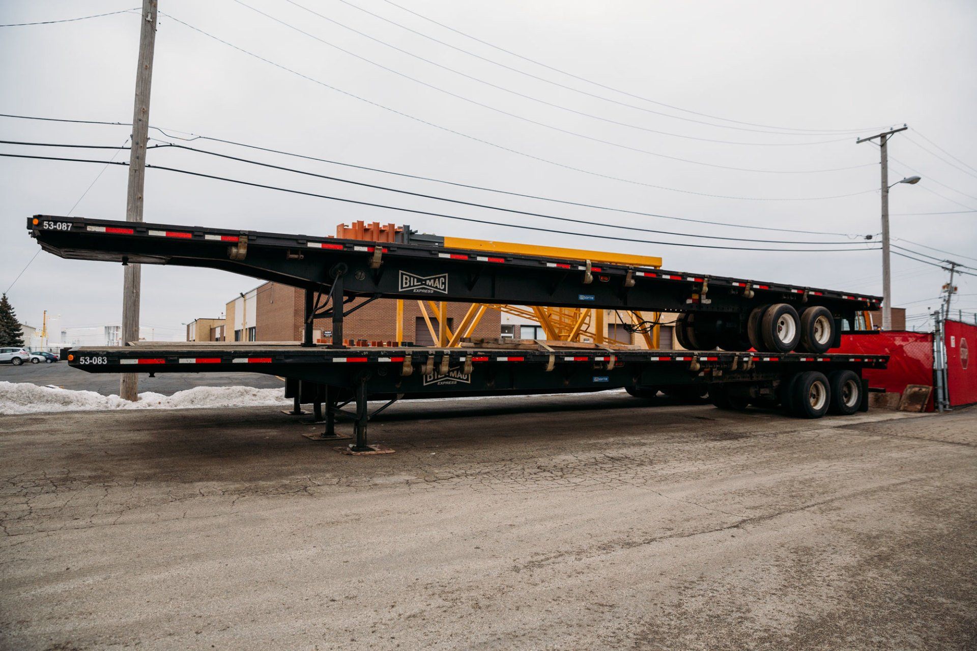 A very long flatbed trailer is parked in a parking lot