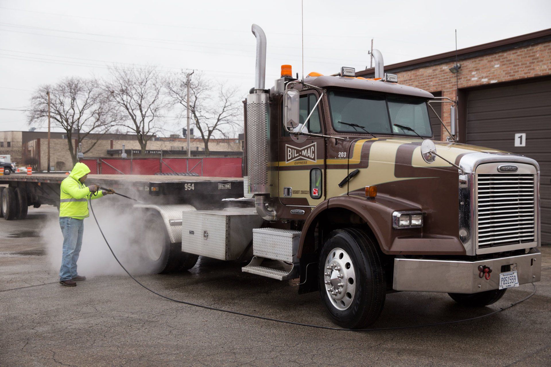 A man is washing a semi truck with a high pressure washer.