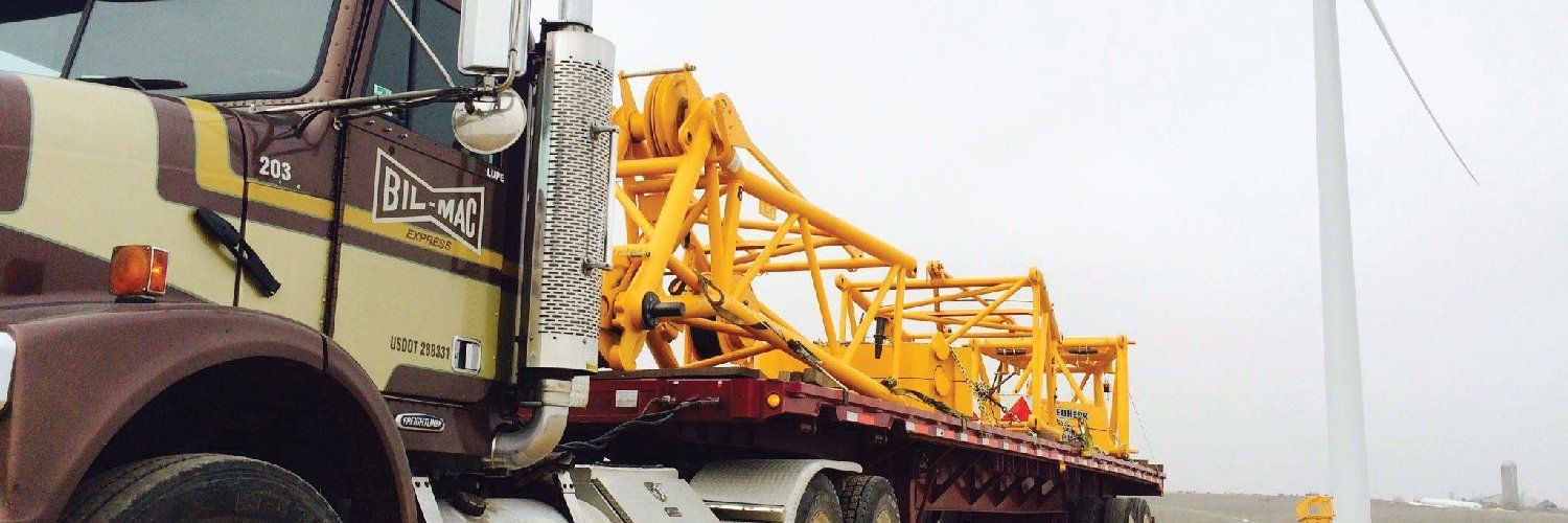 A semi truck is carrying a large yellow crane on a flatbed trailer.