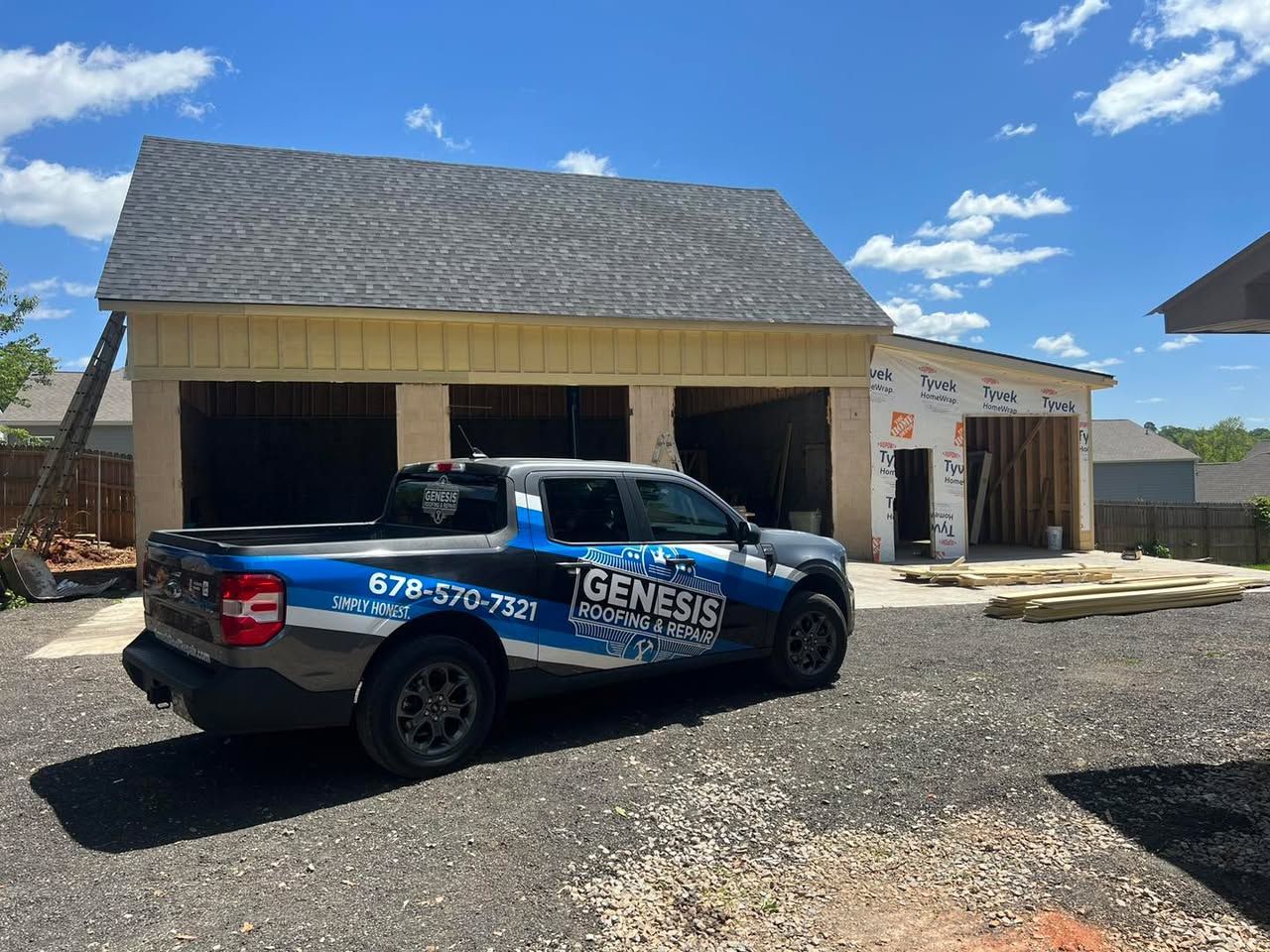 Truck with company logo parked in front of a partially constructed garage on a gravel lot.