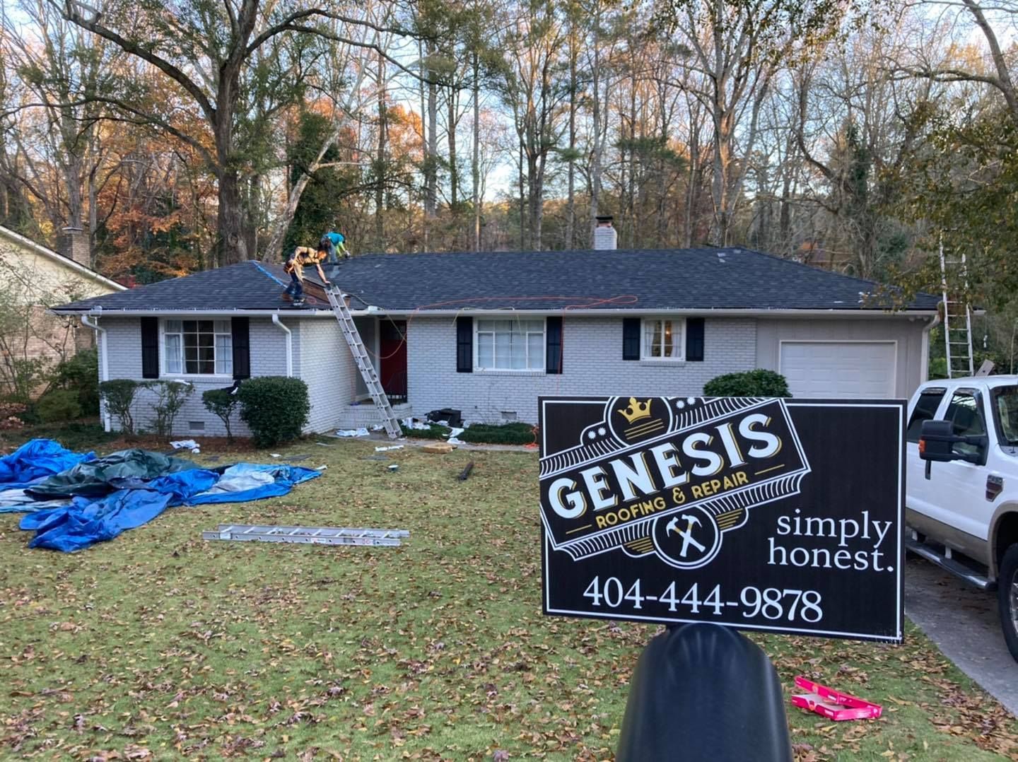 Roofers on a house with a Genesis sign in front; a truck is parked nearby.