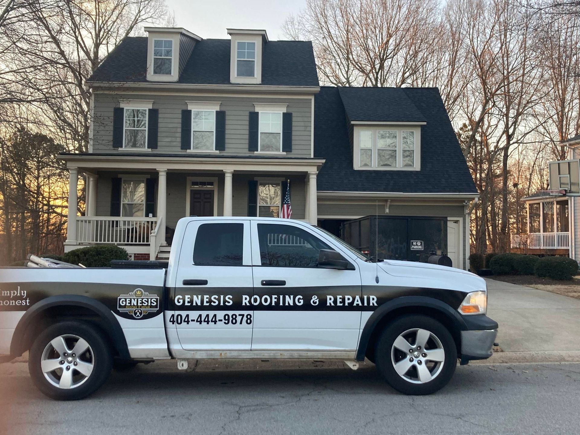 White Genesis Roofing & Repair truck parked in front of a two-story gray house with a black roof.