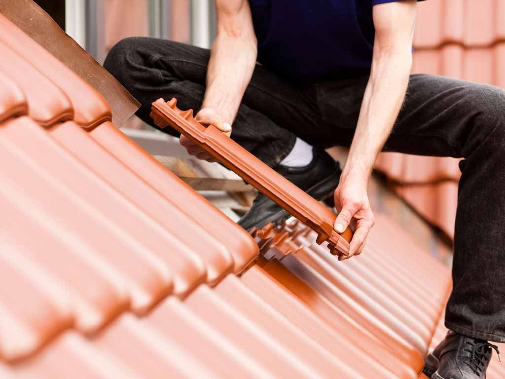Roofer installing a terra cotta roof tile, kneeling on the roof.
