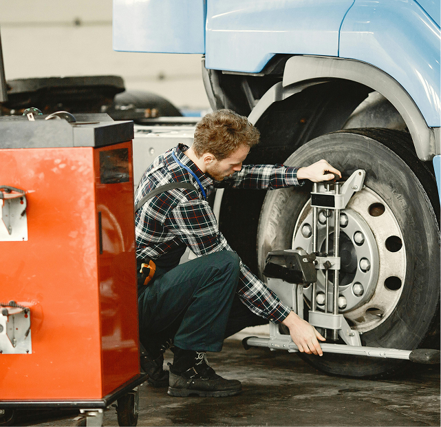 Mechanic adjusting a truck wheel in a repair shop, with tools and a red service cabinet nearby