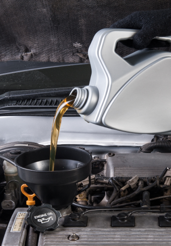 Oil being poured from a jug into a funnel in a car engine bay.