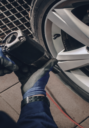Mechanic using a power tool near a car wheel in a garage