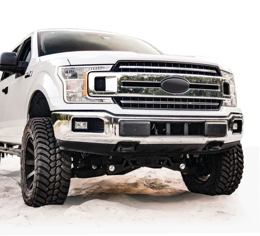 White lifted Ford pickup truck with off-road tires, front view, parked on snow