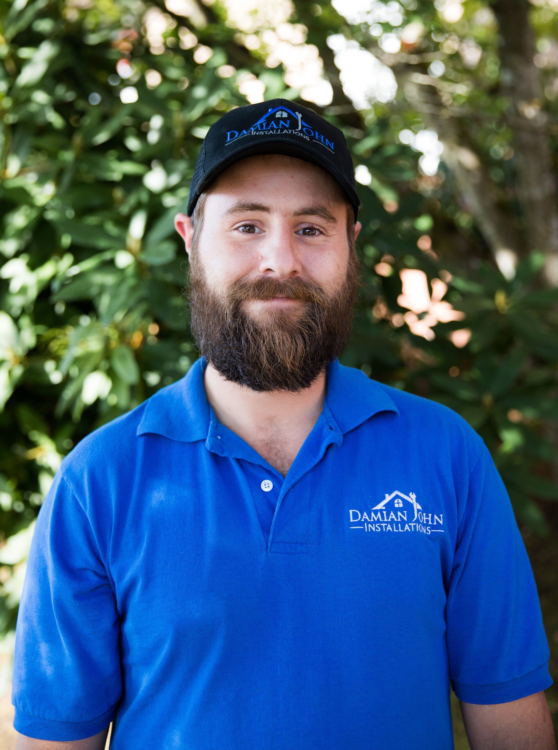 A man with a beard is wearing a blue shirt and a black hat.