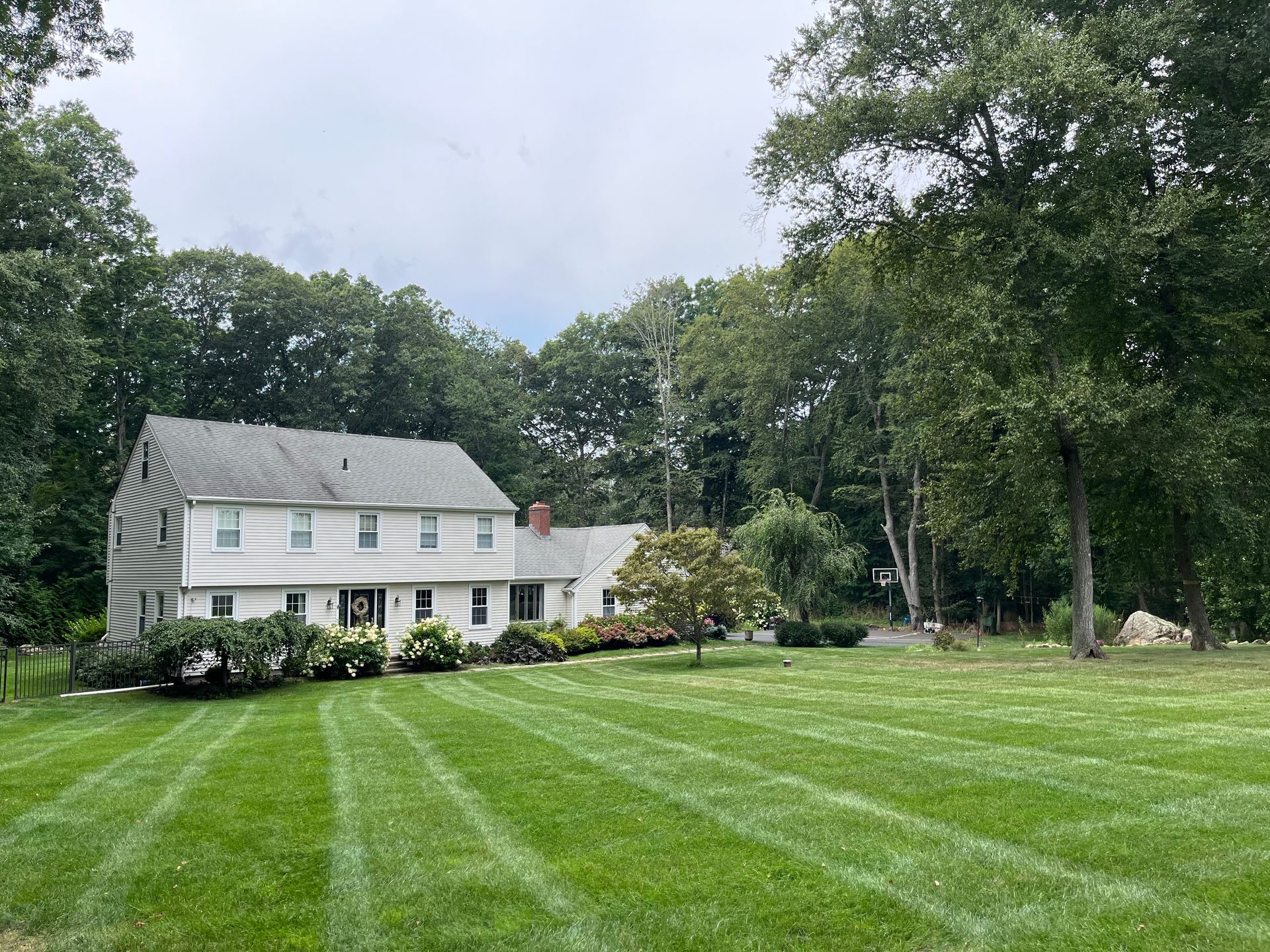 A white house with a large lawn in front of it surrounded by trees.