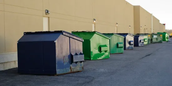 A row of dumpsters are lined up in front of a building.