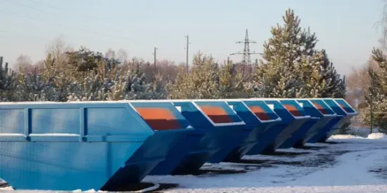 A row of blue dumpsters are lined up in the snow.