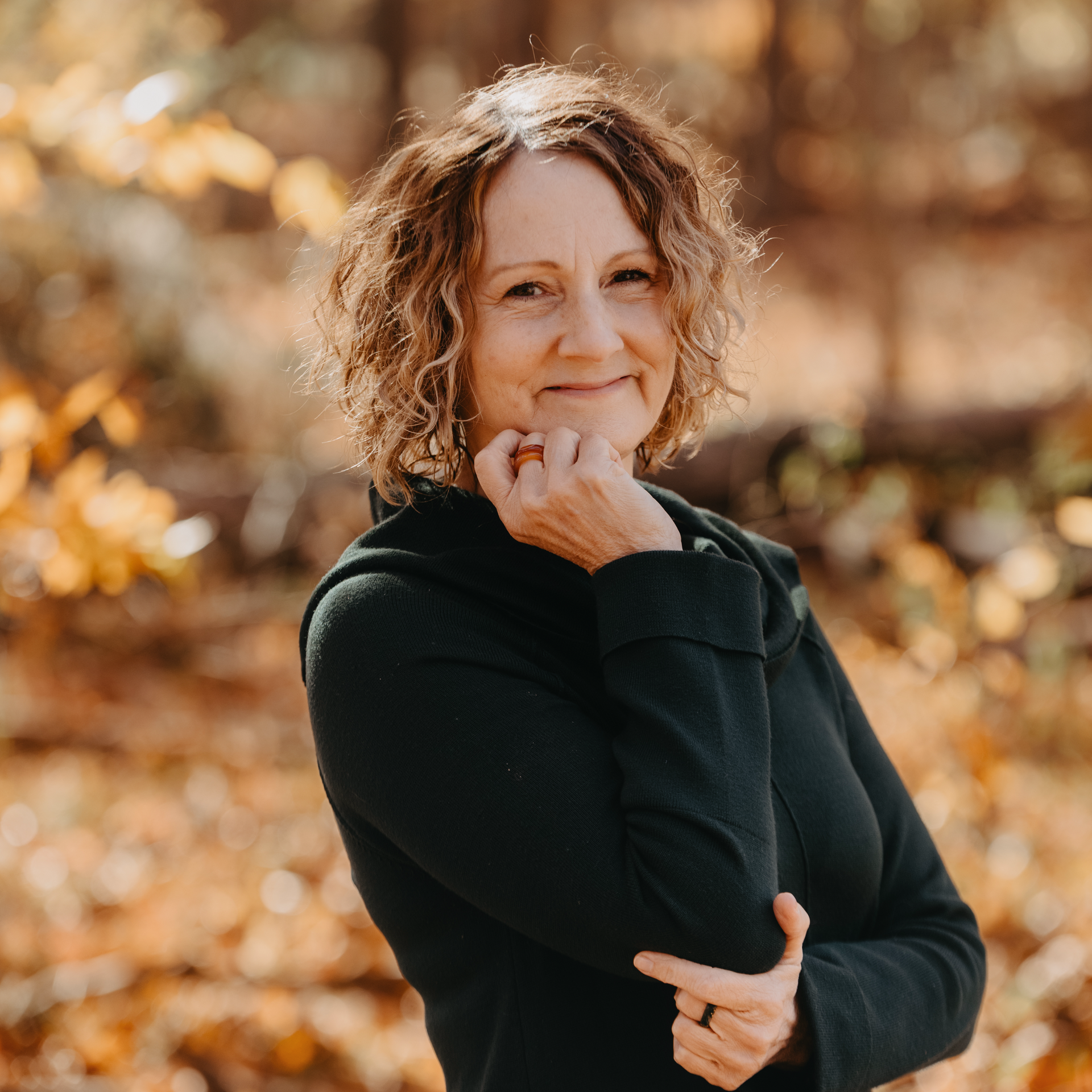 A woman with curly hair is smiling and holding her hand to her chin.