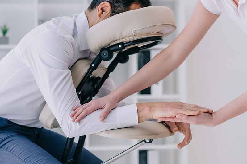 A man is sitting in a chair getting a massage from a woman.