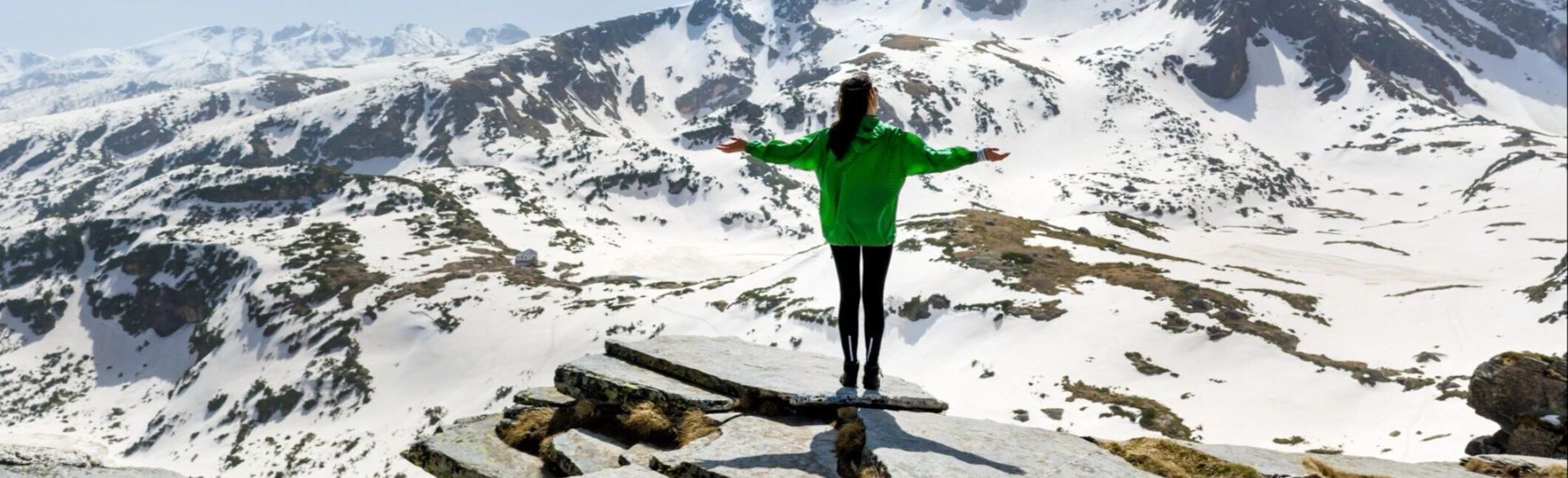 A woman in a green sweater is standing on top of a snow covered mountain.