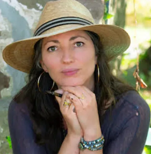 A woman wearing a hat and earrings is sitting in front of a tree.