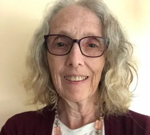 A woman wearing glasses and a necklace is smiling for the camera.